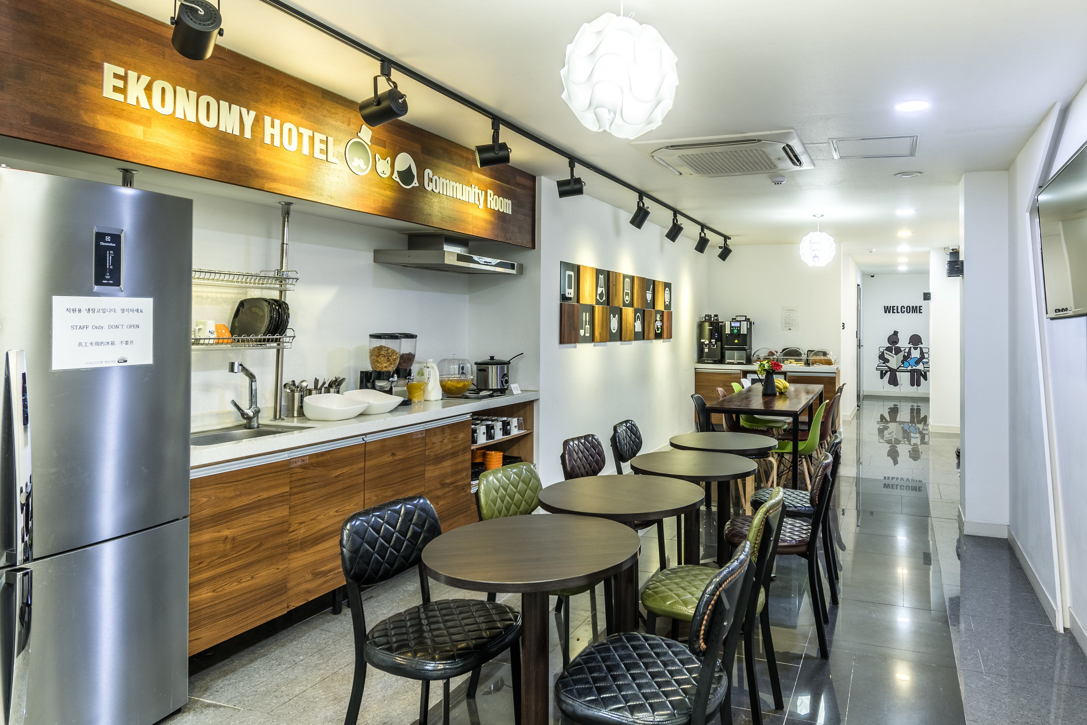 A modern hotel kitchen with stainless steel appliances, wooden cabinets, and a community room sign.