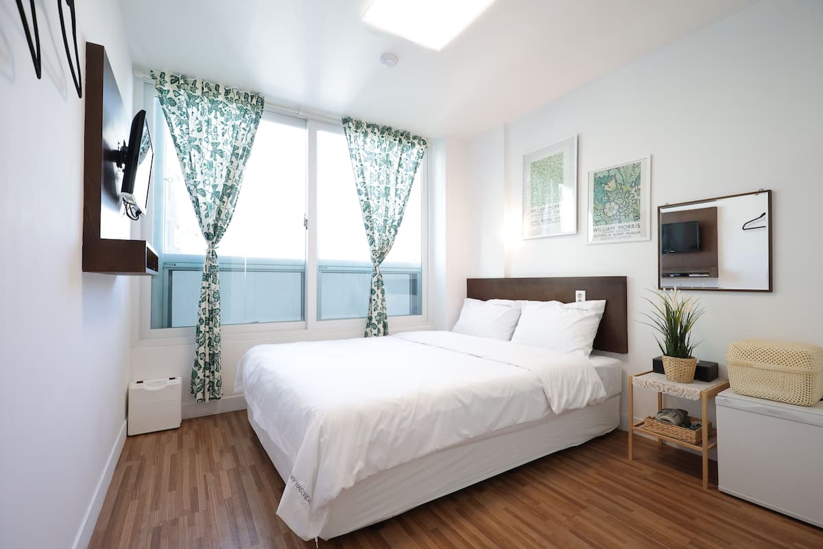 Un dormitorio con una cama grande, un televisor montado en la pared y una mesita con una planta.