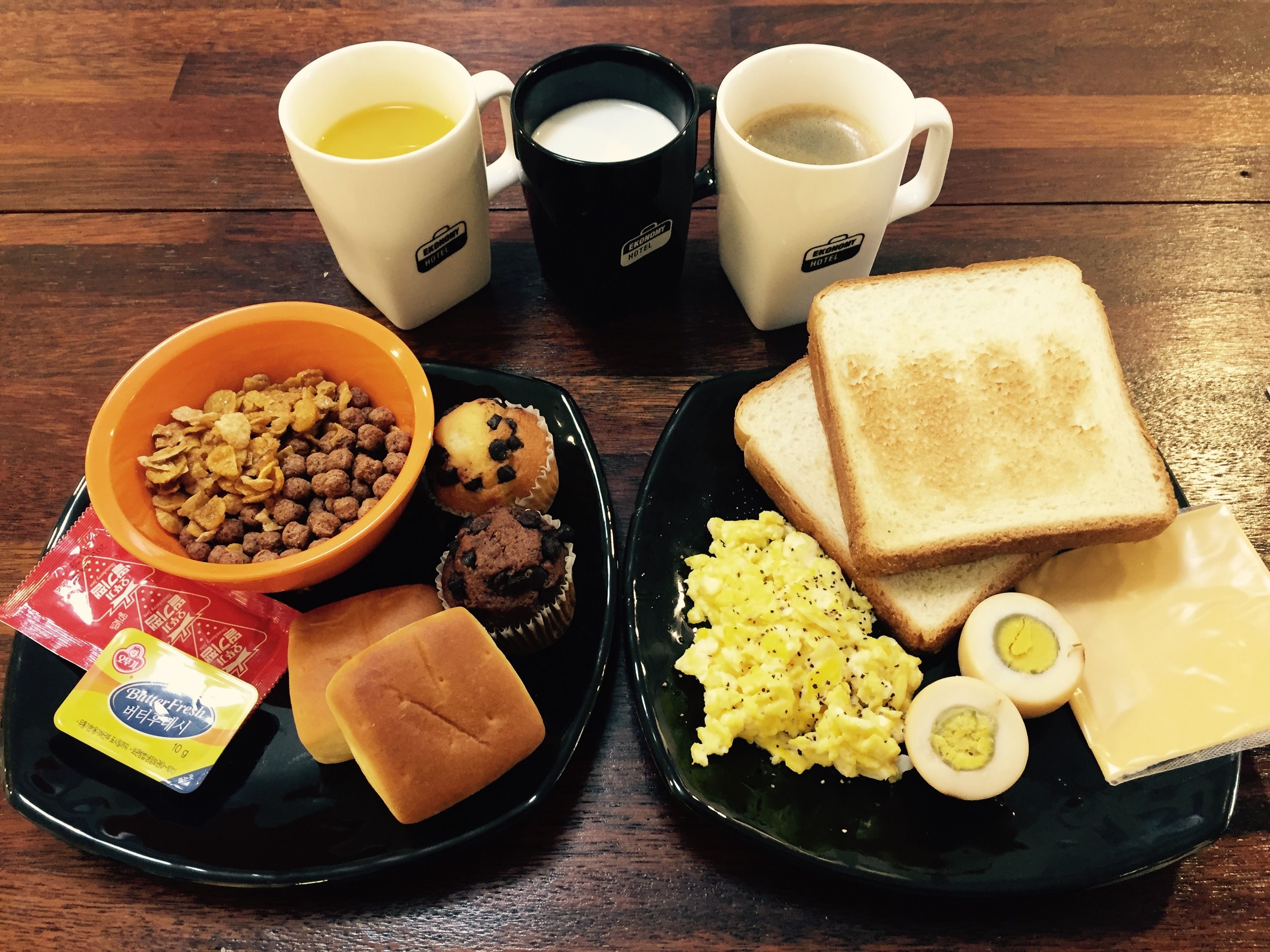 A breakfast plate with toast, eggs, cheese, and a bowl of cereal.