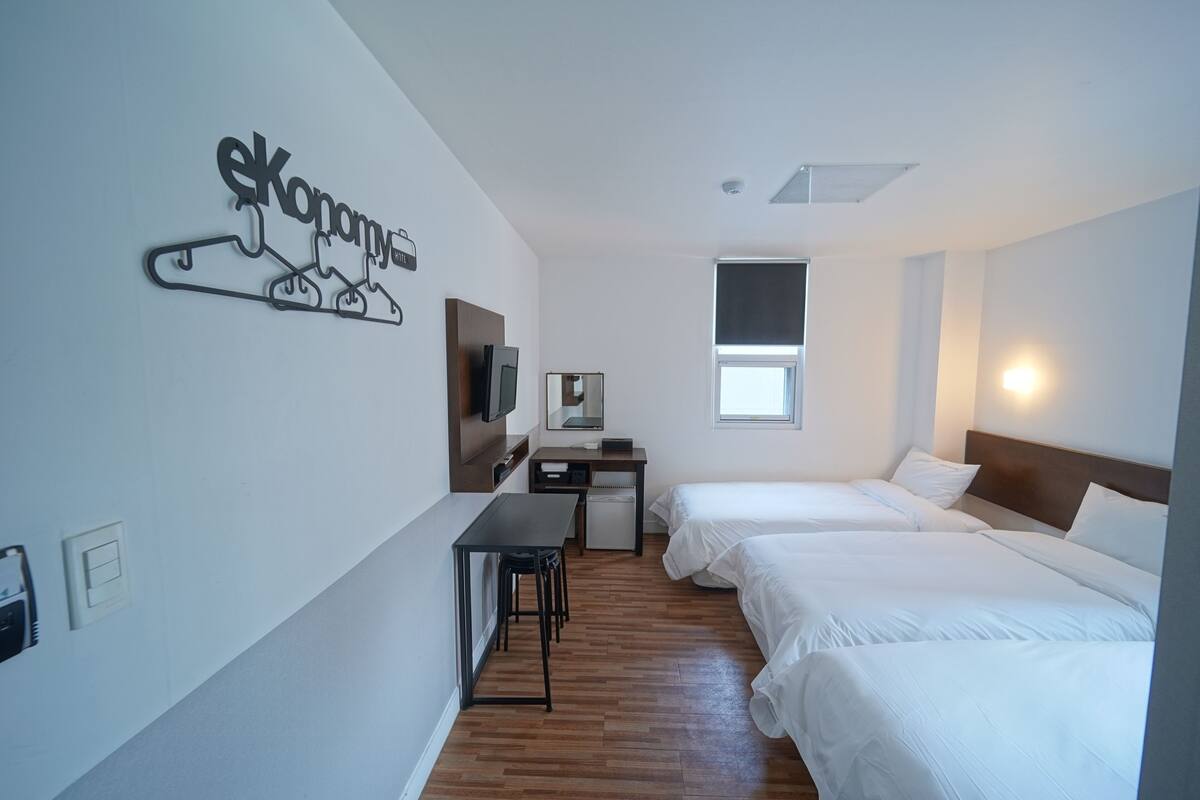 Habitación de hotel con dos camas, un escritorio, una silla, un televisor y un perchero en la pared.