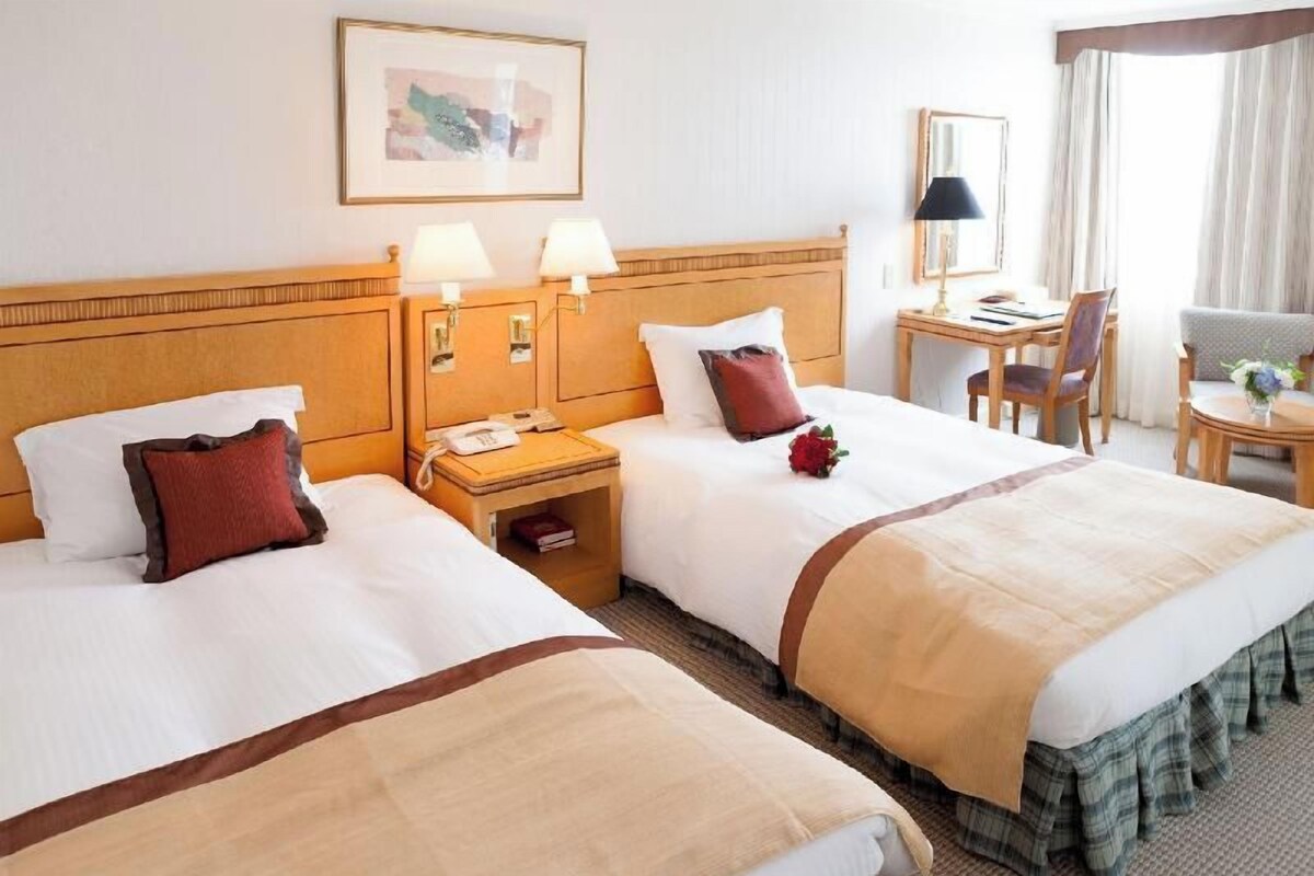 Habitación de hotel con dos camas, un escritorio, una silla, una lámpara y un cuadro en la pared.