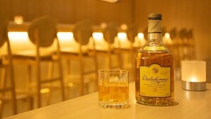 A bottle of Dalwhinnie whisky and a glass on a table in a warmly lit room with chairs and a candle. - Wishton Hotel Yukari (Sakura)