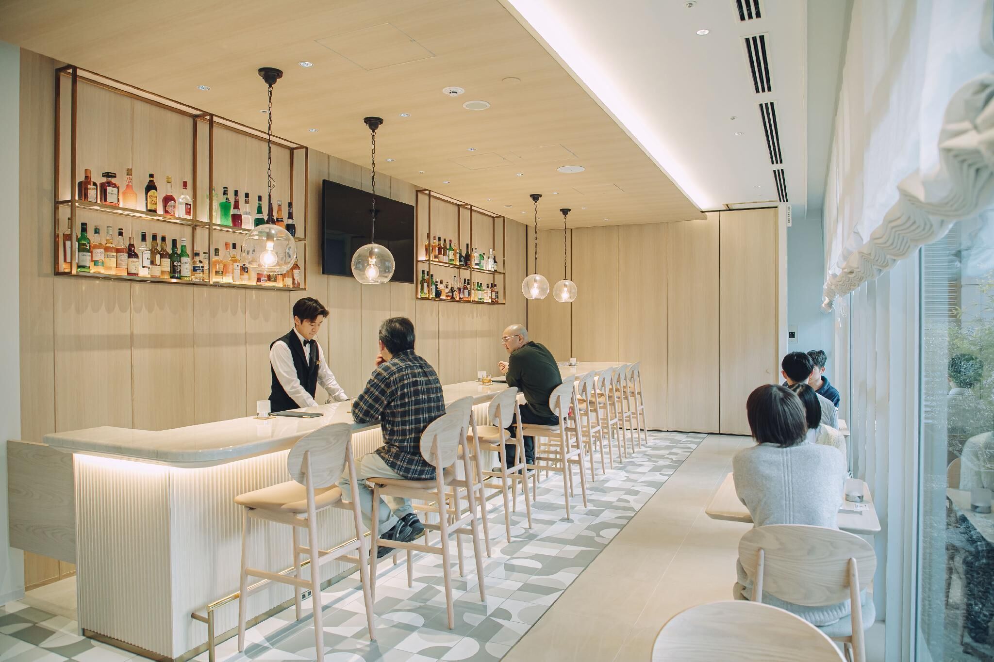 A modern bar area with wooden paneling, a variety of liquor bottles, and a seating arrangement with bar stools and tables.