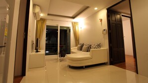 Un salon moderne avec un canapé blanc, une petite table d’appoint et une porte vitrée donnant sur un balcon.