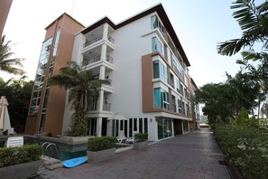 A modern multi-story hotel with balconies, a swimming pool, and lush greenery.