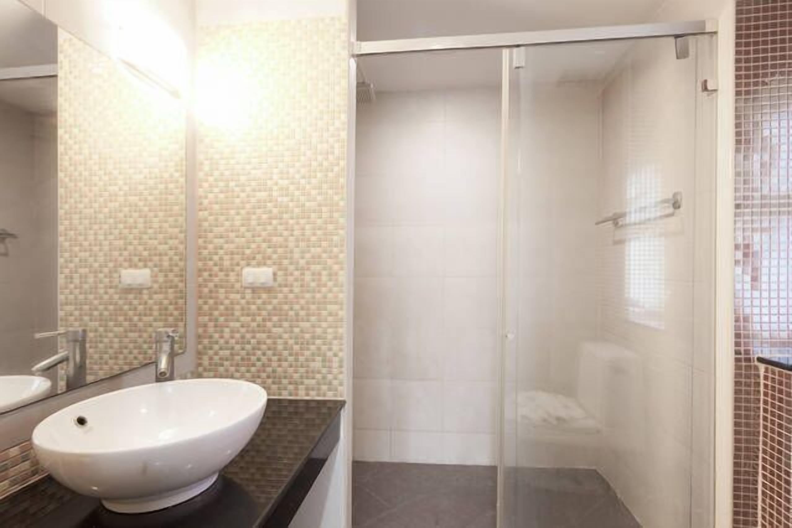 Casa de banho com lavatório branco, espelho e cabine de duche em vidro.