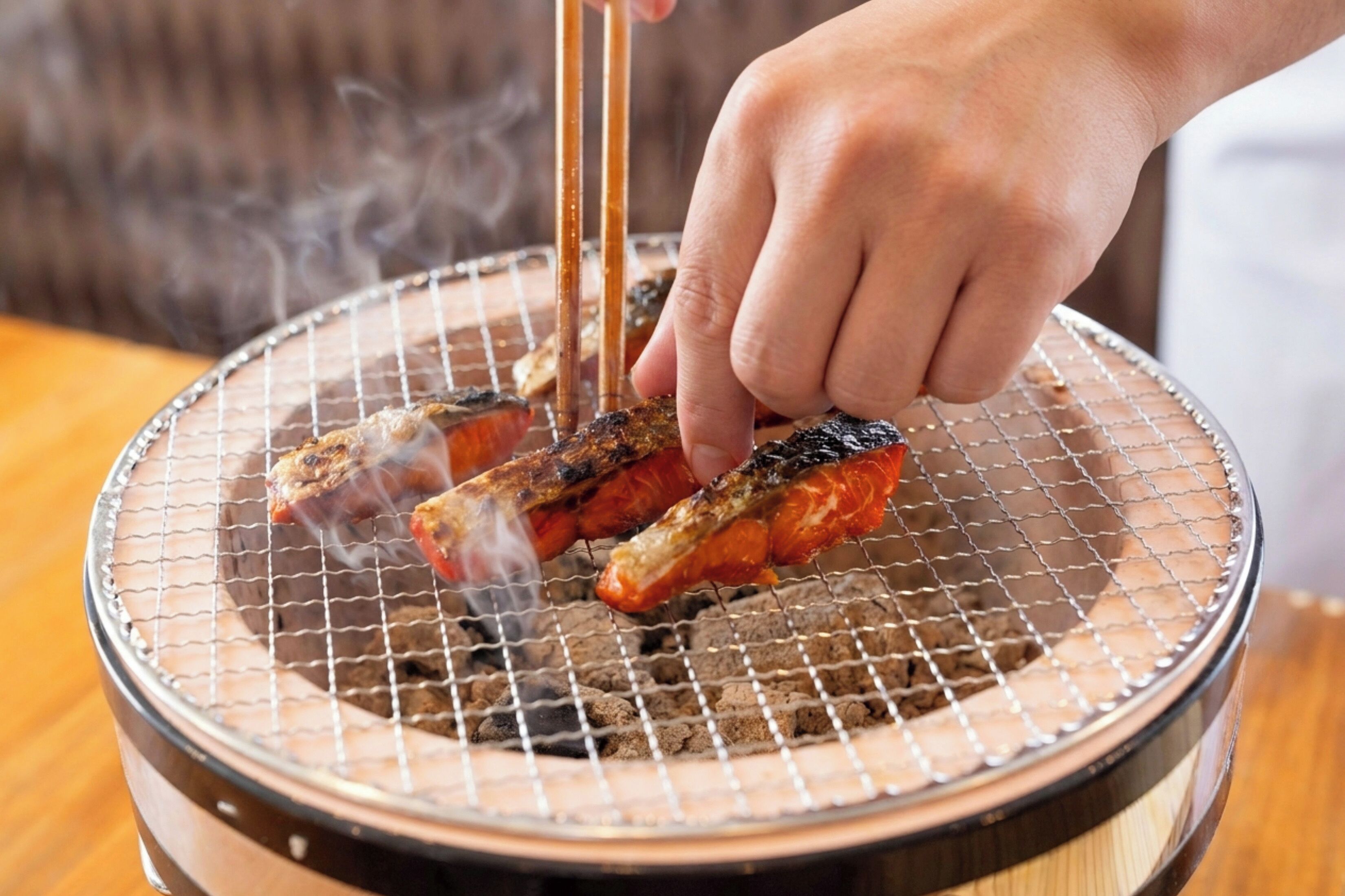 Eine Hand grillt Essen auf einem Drahtrost über einem Holzkohlegrill.