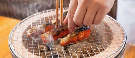 Eine Hand grillt Essen auf einem Drahtrost über einem Holzkohlegrill.