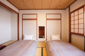 Habitación de hotel con dos camas, techo de madera y puerta corredera tradicional japonesa.