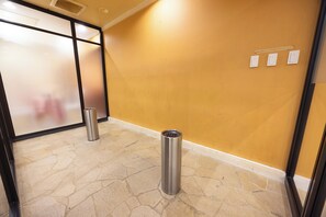 A hallway with a tiled floor, a trash bin, and a wall with three light switches.