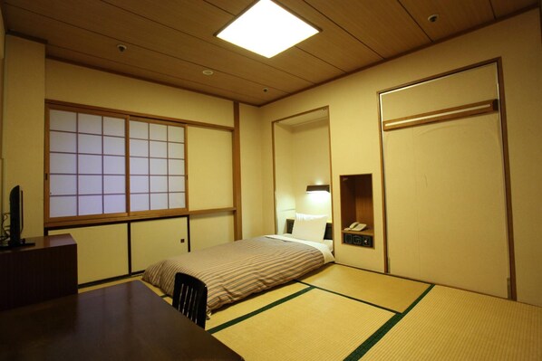 Una habitación japonesa tradicional con suelo de tatami, una cama, un escritorio y una puerta corredera.