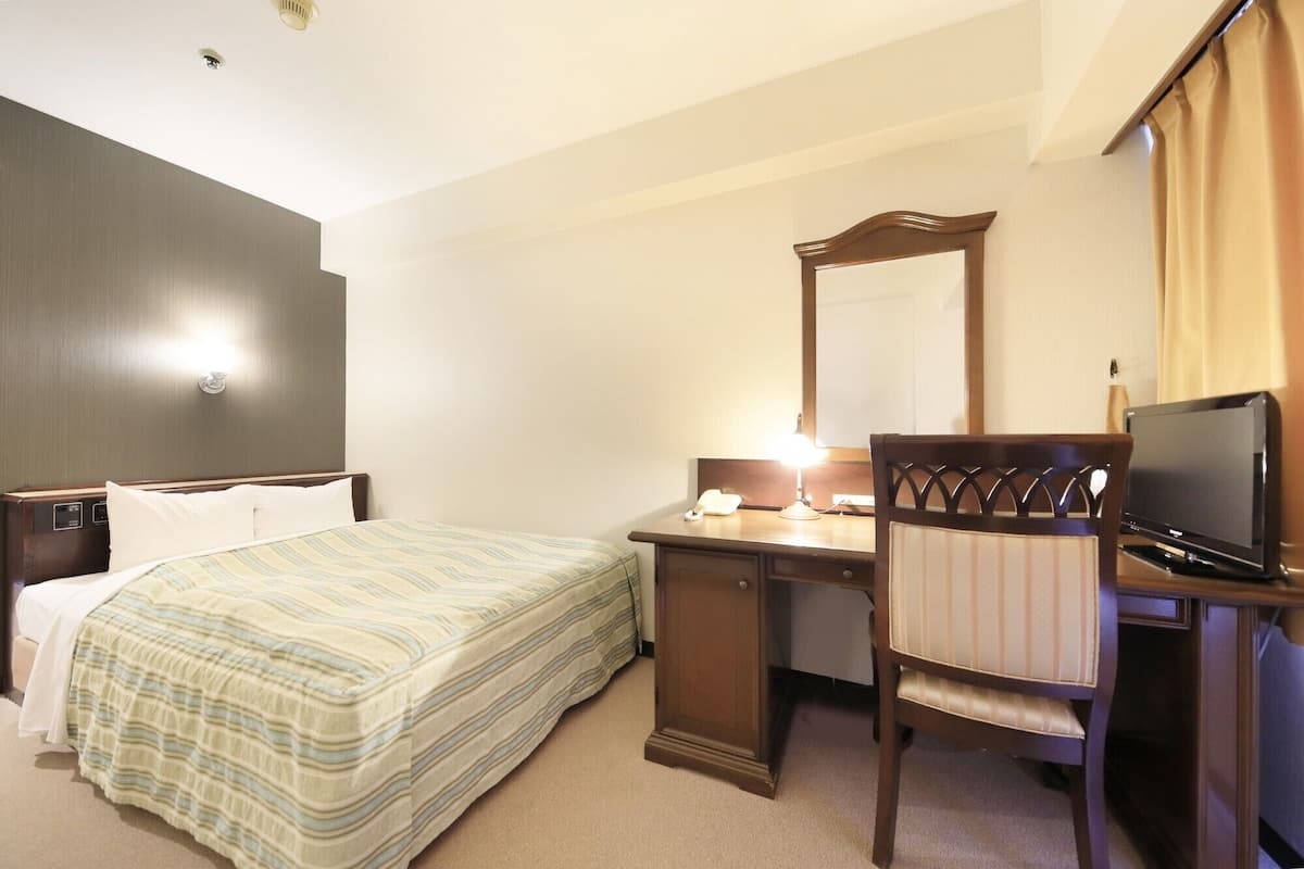 Una habitación de hotel con cama, escritorio, silla, televisor y espejo.