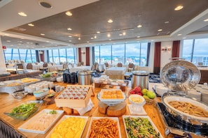 A buffet setup in a room with multiple tables, a large window offering a city view, and a ceiling with recessed lighting. - Hirosaki Park Hotel (Hirosaki)