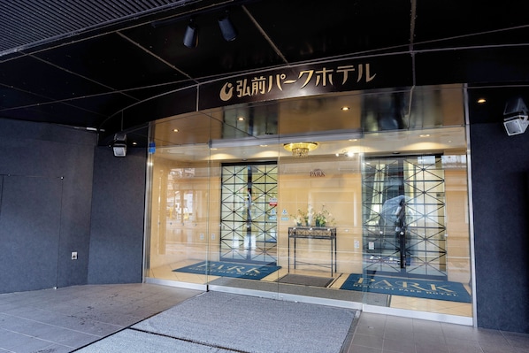 A hotel entrance with a glass facade, a reception desk, and a sign above the door.
