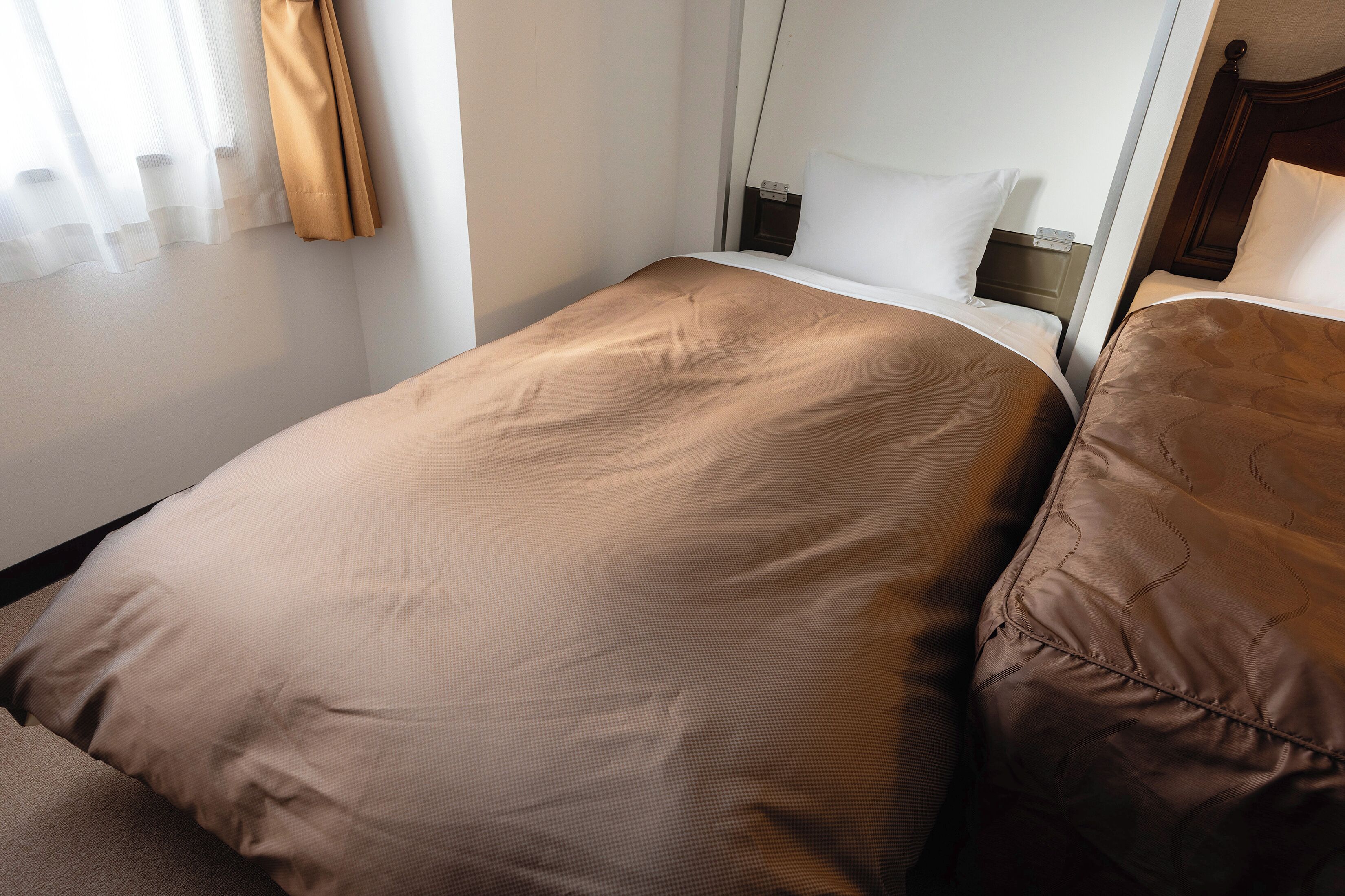 A single bed with a brown bedspread and matching pillow in a hotel room.