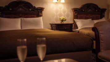 A hotel room with two beds, a nightstand with a vase of flowers, and a table with two glasses of water.