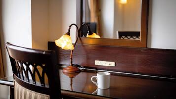 A wooden chair with a cushion, a white mug on a reflective surface, and a wall-mounted lamp with a visible switch.
