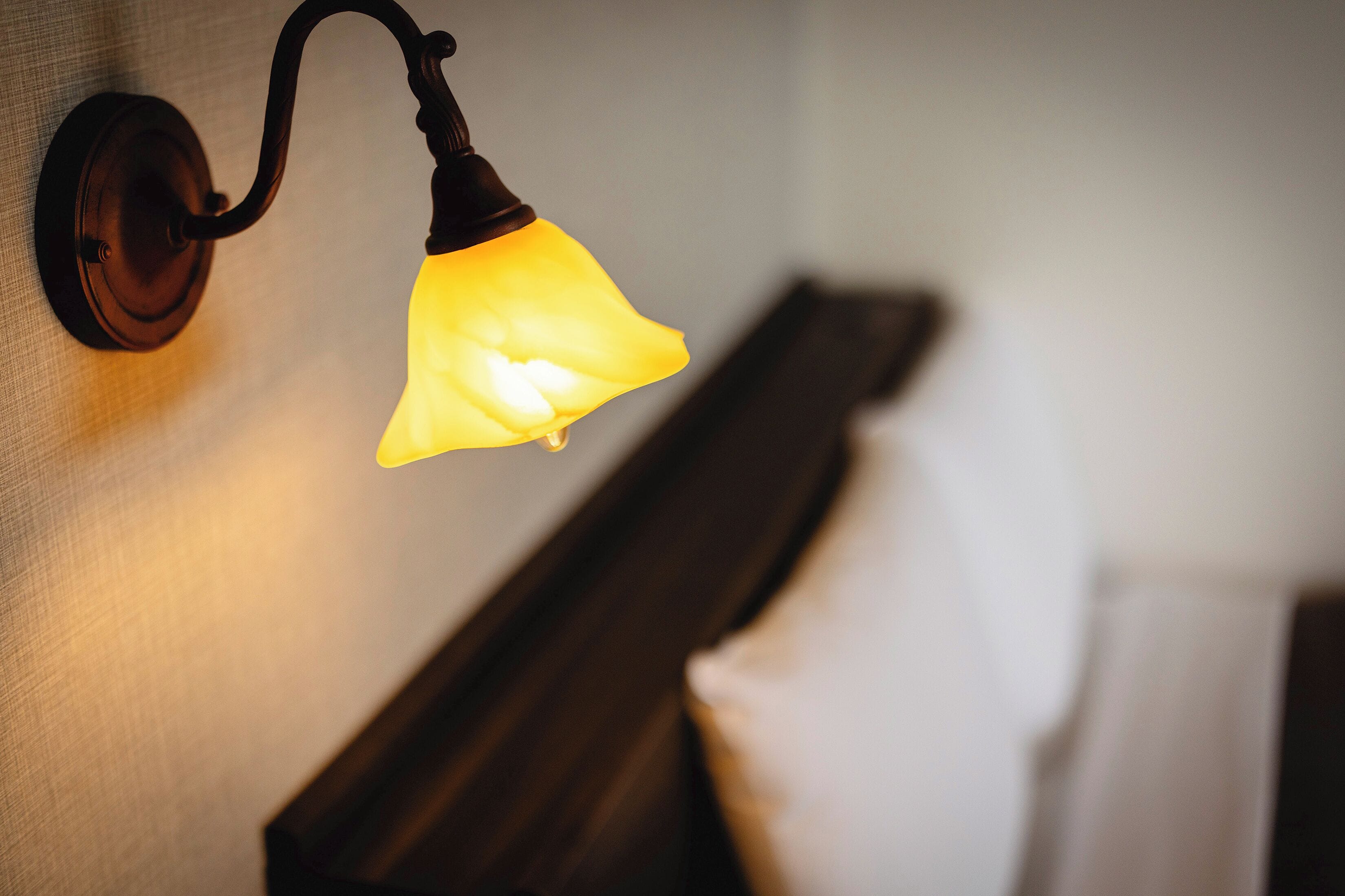 A wall-mounted light fixture with a triangular shade, a wooden headboard, and a white towel.