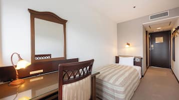 A hotel room with a bed, bedside table, lamp, mirror, and a door leading to another room.