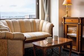 A hotel room with a sofa, a small table with two white mugs, a lamp, and a cabinet with glasses.
