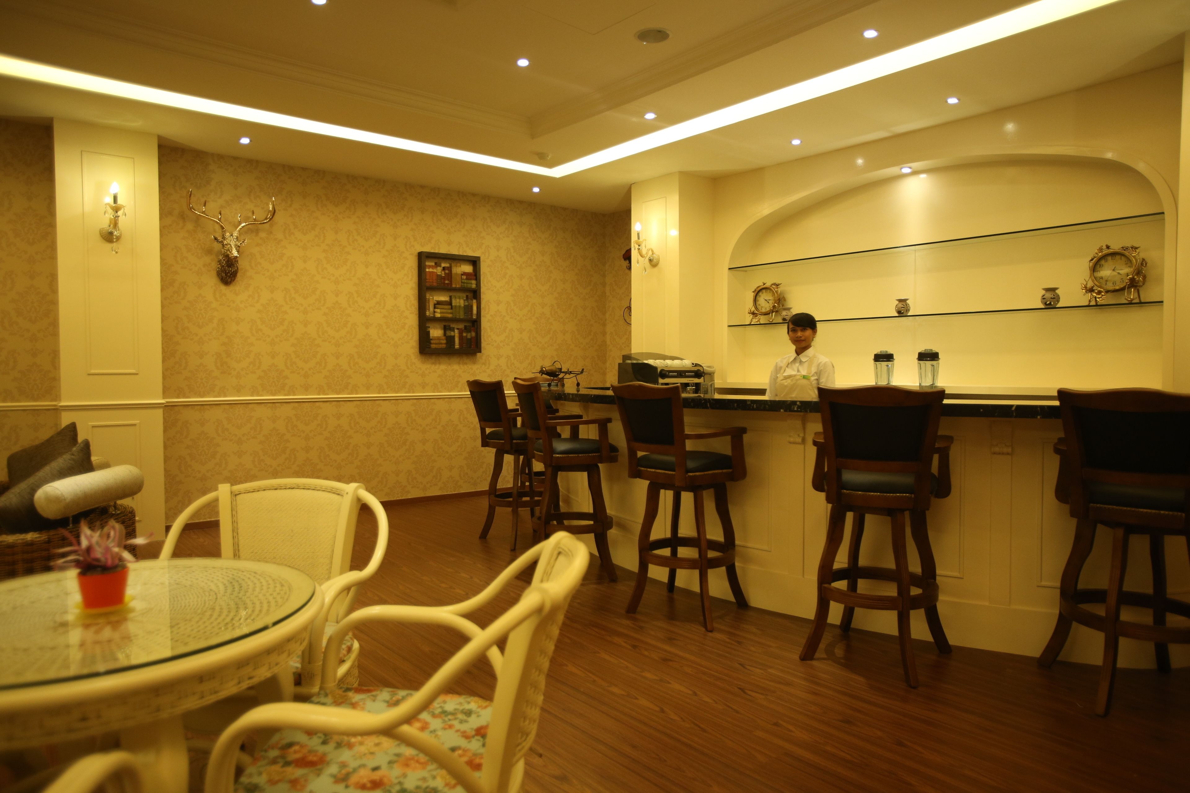 A hotel dining area with a round table, bar stools, and a bartender.