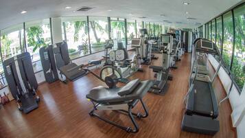 A gym with various exercise equipment, large windows, and a wooden floor.