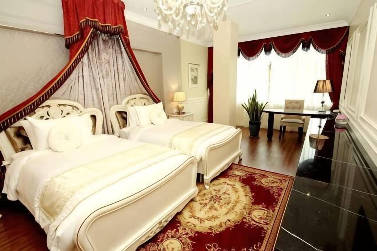 Ein Schlafzimmer mit Himmelbett, einer Kristallleuchter, einem Essbereich und einem roten Teppich.