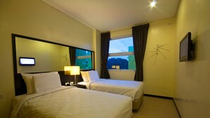 A hotel room with two beds, a TV, a lamp, and a window with curtains.