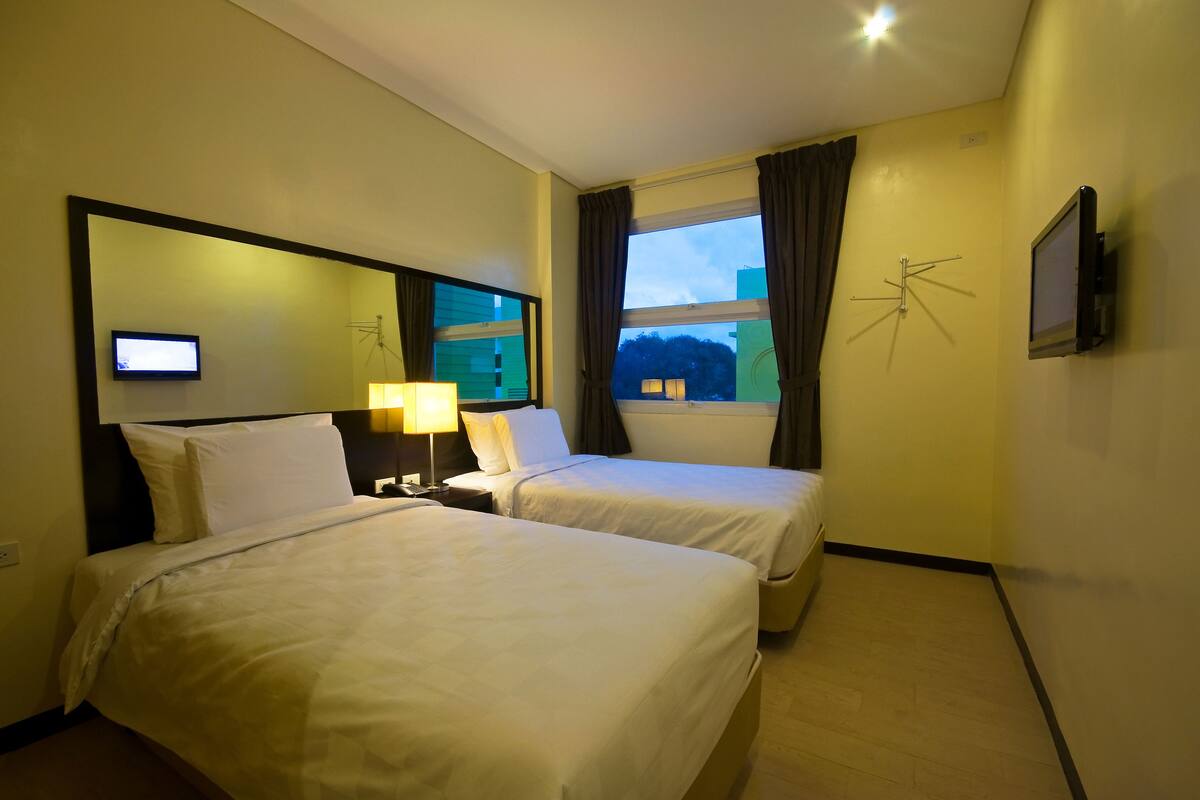 Een hotelkamer met twee bedden, een televisie, een lamp en een raam met gordijnen.