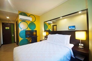 A hotel room with a large bed, a TV, a desk, and a mirror.