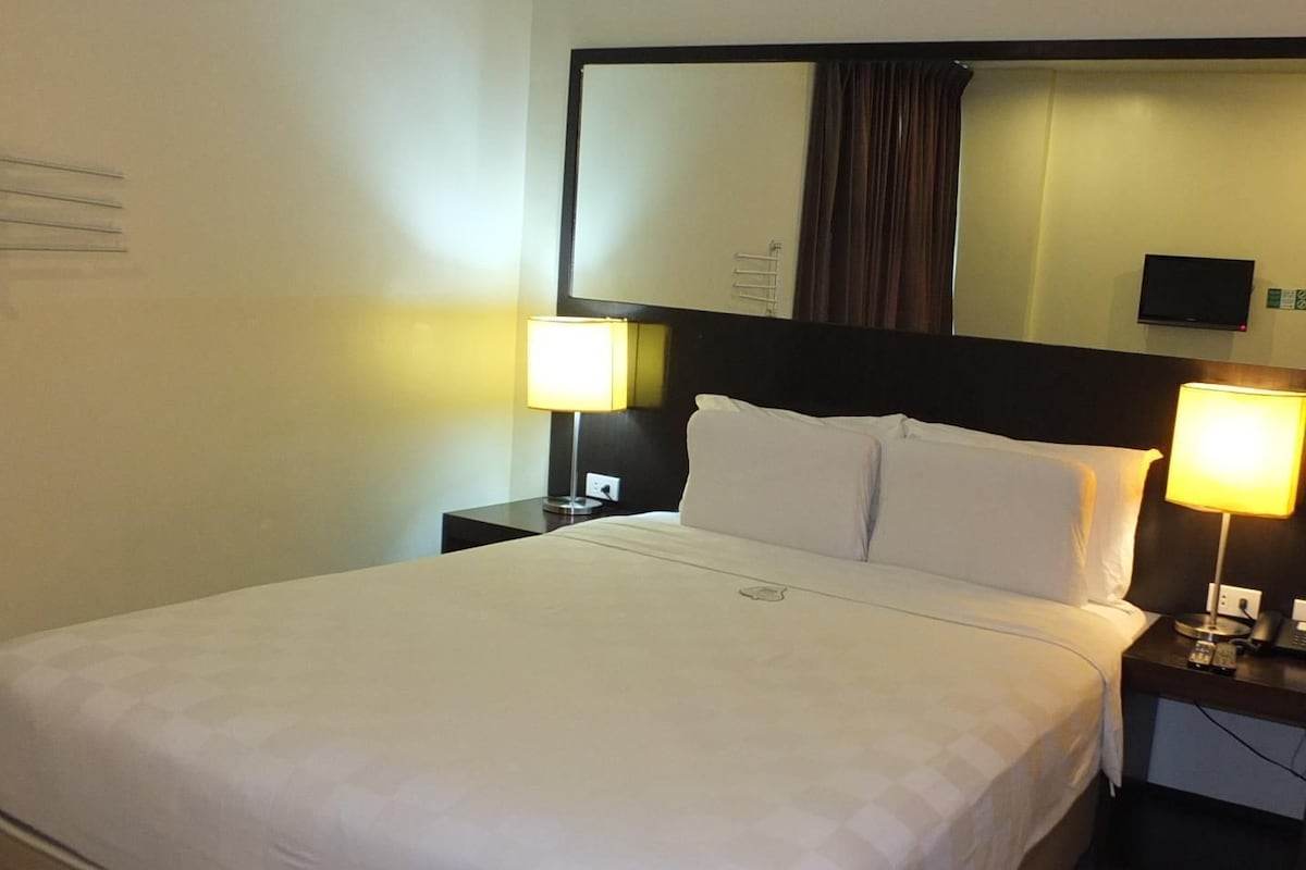 Een hotelkamer met een groot bed, twee nachtkastjes, een spiegel en een televisie.