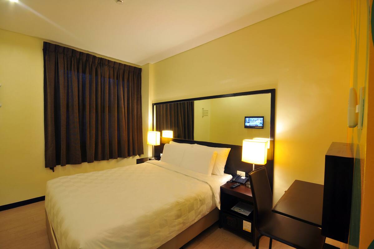 Een hotelkamer met een groot bed, twee bedlampen, een bureau met stoel, en een televisie aan de muur.