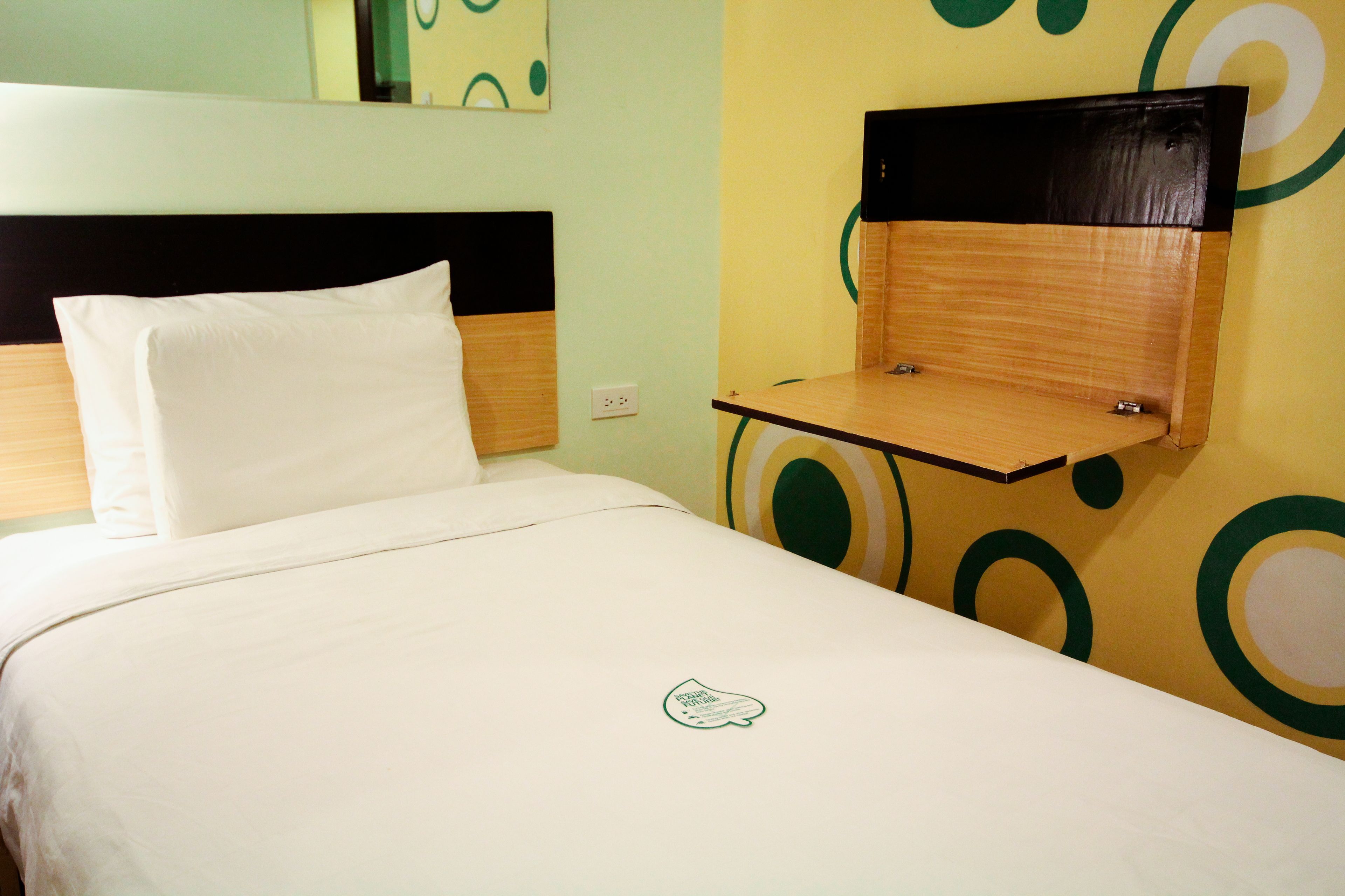 A hotel room with a bed, a wooden nightstand, and a wall with circular patterns.