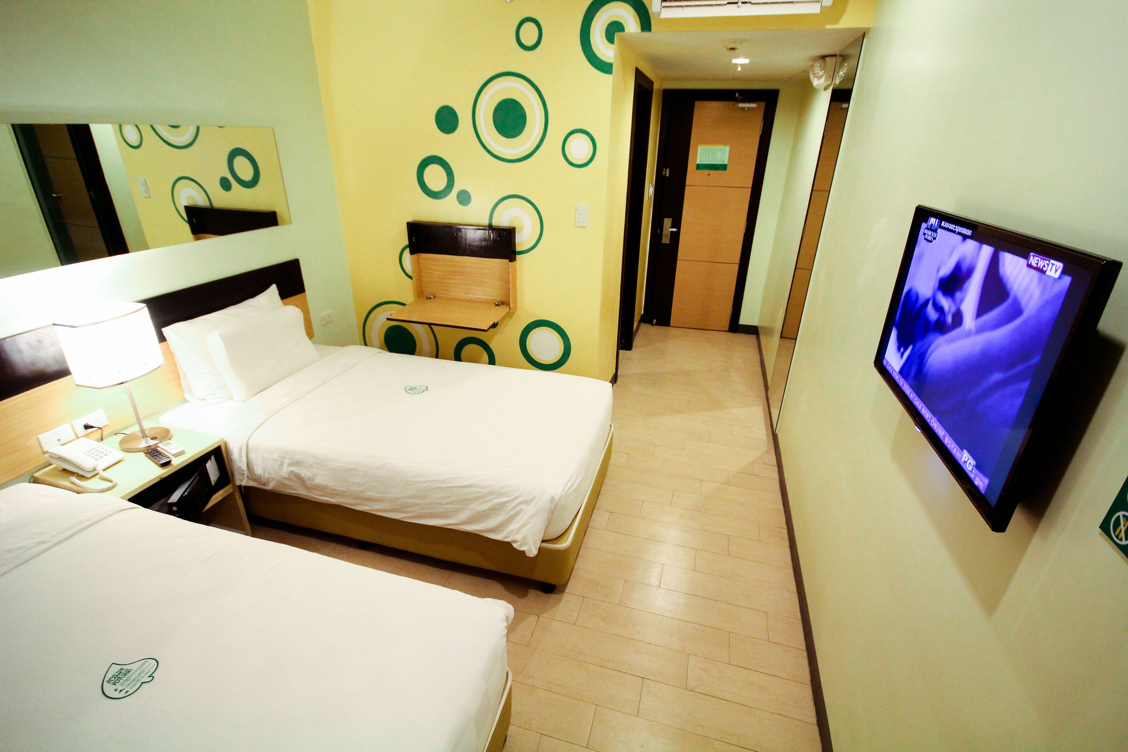 A hotel room with two beds, a TV on the wall, a mirror, and a door leading to another room.