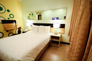 Una habitación de hotel con una cama grande, mesitas de noche, un espejo y un televisor.