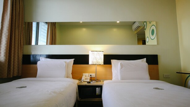 A hotel room with two beds, a nightstand with a lamp, a mirror, and a wall-mounted air conditioner. - Go Hotels Iloilo (Iloilo)