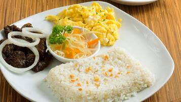 A plate of food with rice, scrambled eggs, beef, and onions on a wooden table.