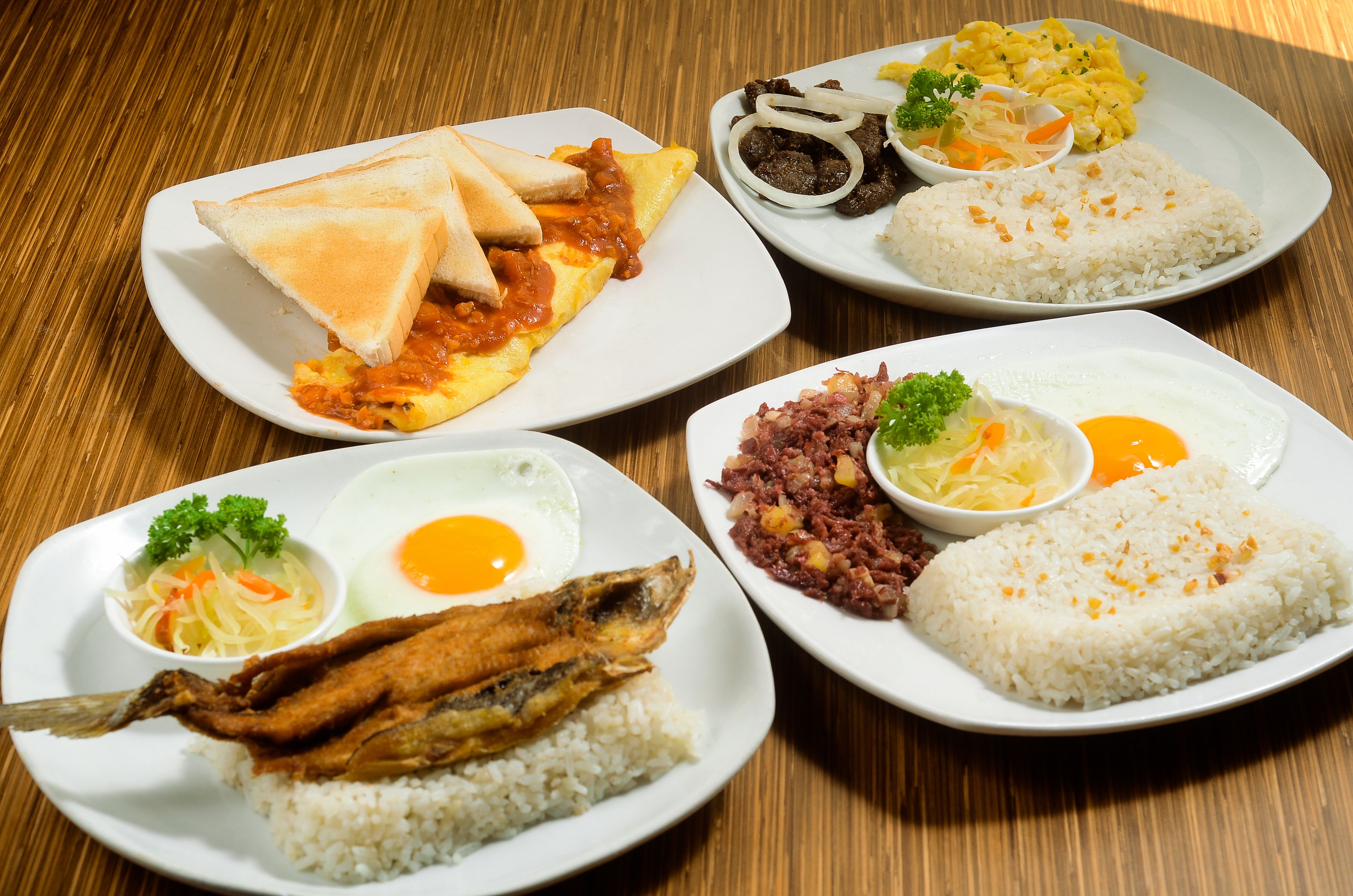 A wooden table with four plates of food.