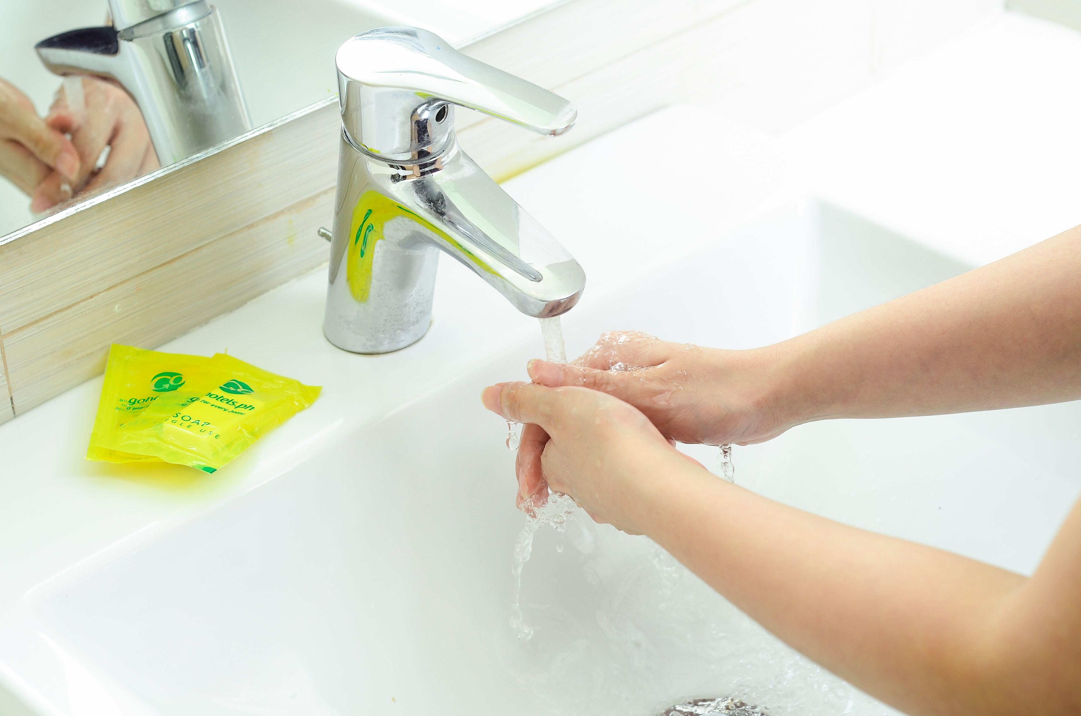 A bathroom sink with a faucet, a yellow soap packet, and a mirror reflecting a hand washing.