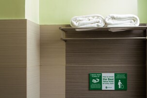 A hotel bathroom with a towel rack holding folded towels and a sign requesting new towels.