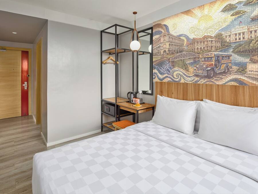 A hotel room with a bed, a desk, a hanging light fixture, and a wall mural.