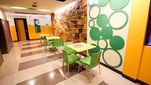 A hotel lobby with green chairs and tables, a stone wall, and a yellow accent wall with green circles. - Go Hotels Iloilo (Iloilo)