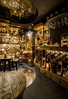 A bar area with shelves of bottles, a wooden bar counter, and a seating area with stools.