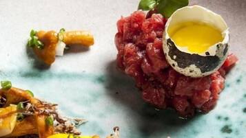 A plate with a dish of raw meat, a cracked egg, and some garnishes.