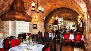 A restaurant with brick walls, white decorative panels, and red upholstered chairs. Tables are set with white tablecloths and silverware.