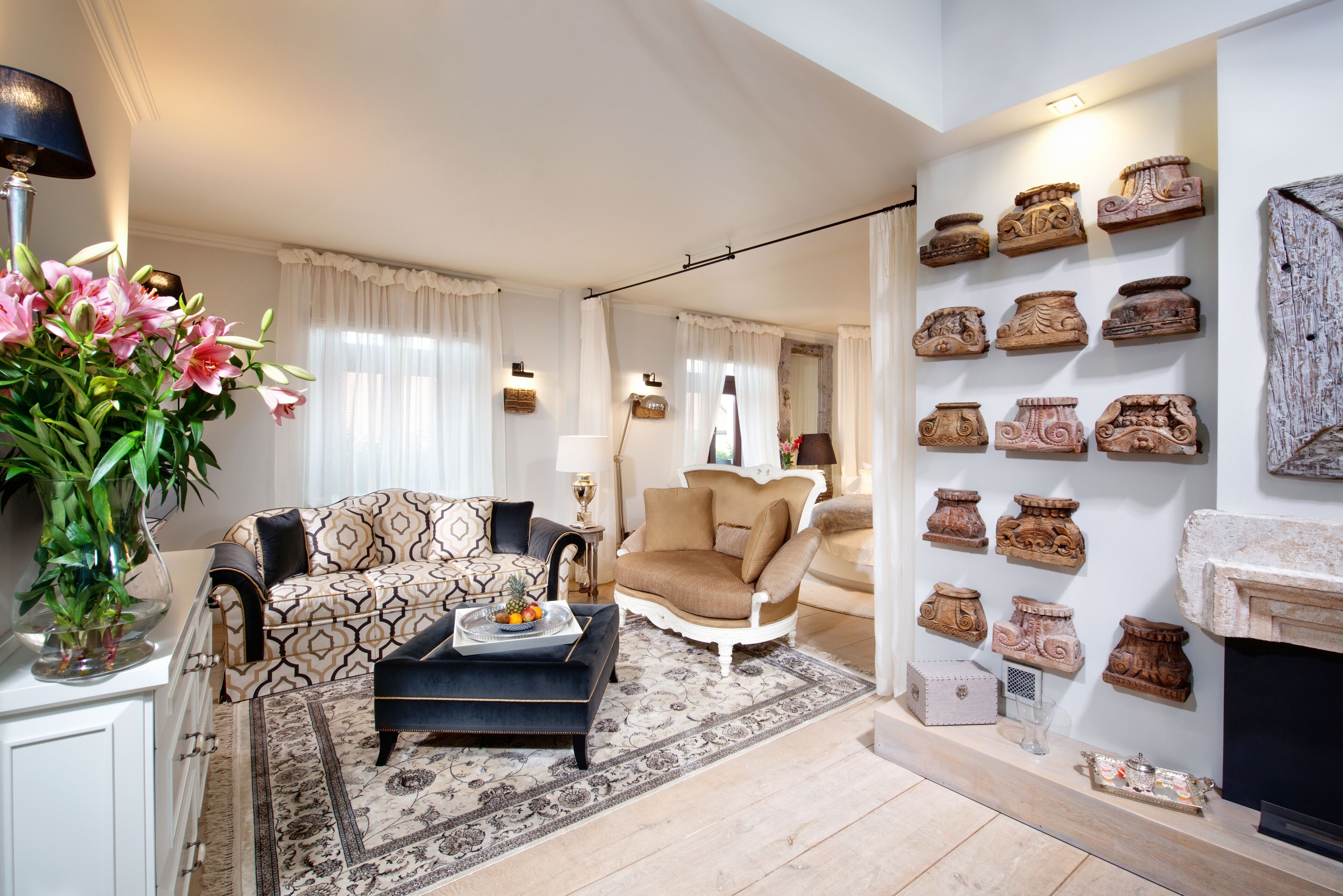 A living room with a patterned sofa, a black ottoman, a decorative vase, and a wall display of pottery.