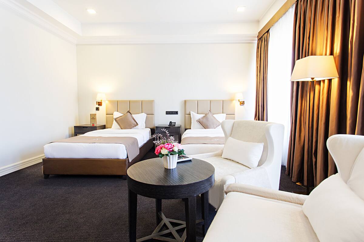 Habitación de hotel con dos camas, un sofá, una mesita con un florero y una lámpara.