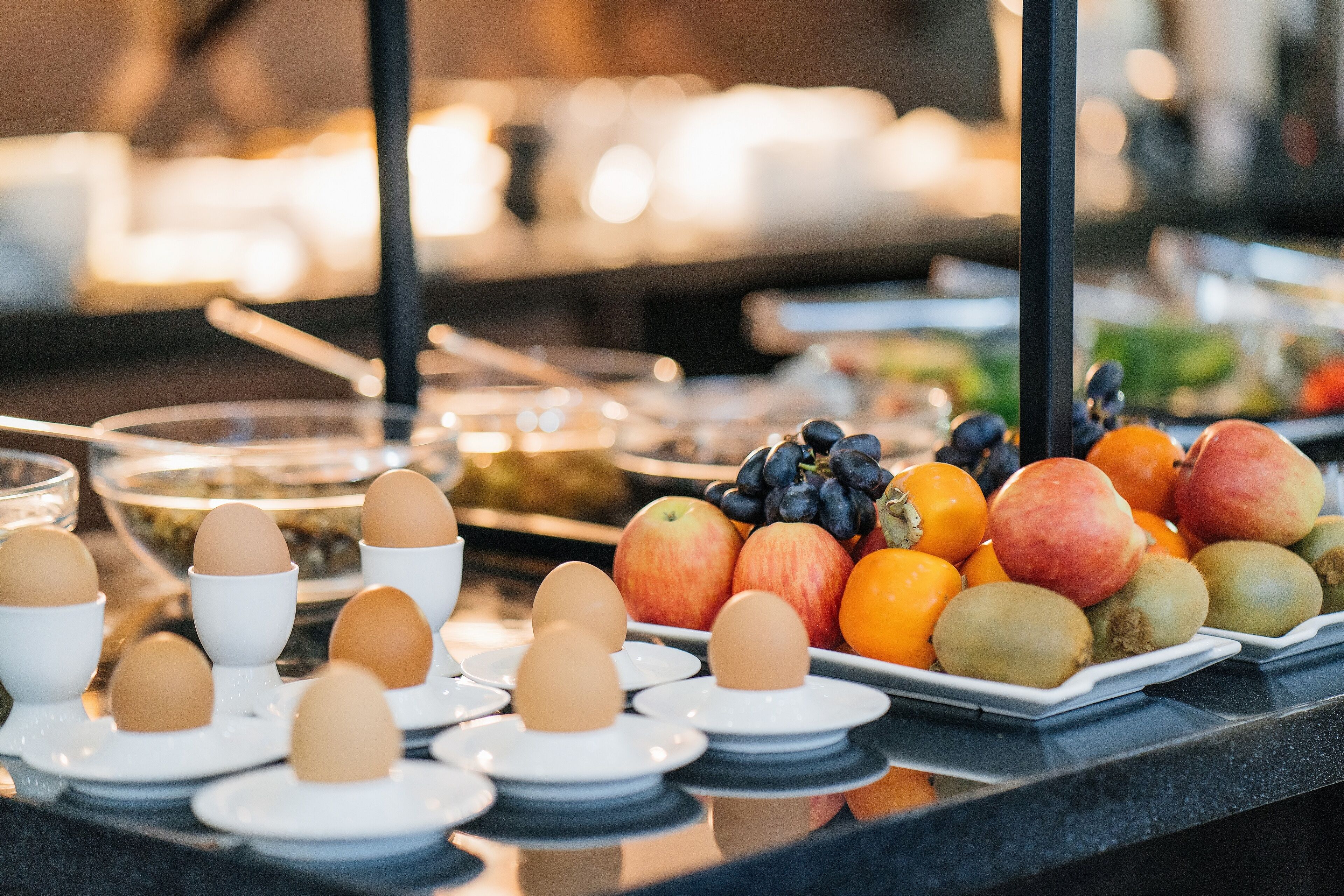 A buffet with various food items including eggs, apples, oranges, and grapes.