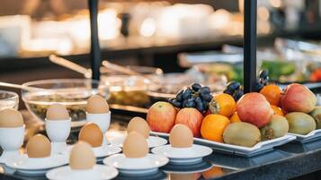 A buffet with various food items including eggs, apples, oranges, and grapes.