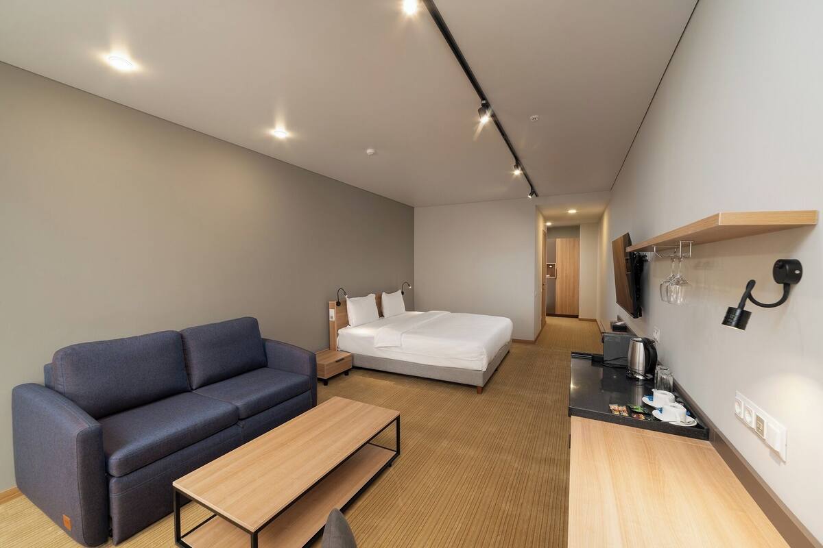 Una habitación de hotel moderna con sofá, cama, una mesita y una kitchenette.